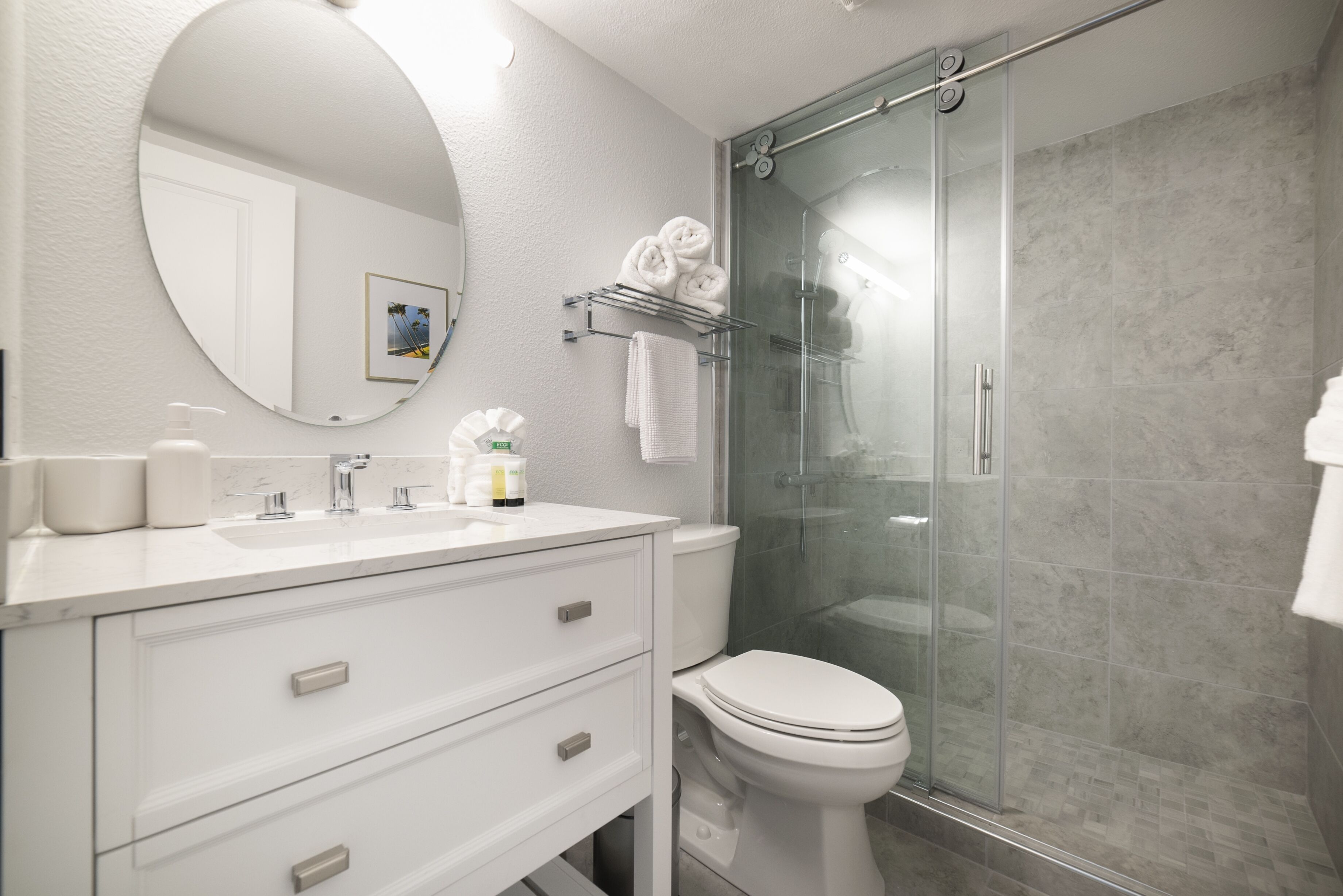 Une salle de bain moderne avec un meuble-lavabo blanc, un miroir rond, des toilettes et une douche à parois de verre.