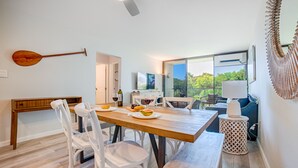A modern dining area with a wooden table, white chairs, and a view of the outdoors. - Ocean view, fully remodeled, 2nd floor, few steps away from the best beaches (Kihei)