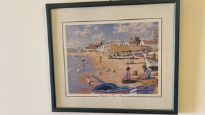 A framed painting of a beach scene with people, boats, and buildings. - Algarve, T2 apartment w/balcony, Armação de Pera (Armação de Pêra)