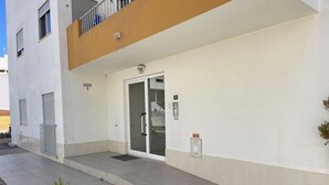 A building entrance with a glass door, a small planter with plants, and a sign on the wall. - Algarve, T2 apartment w/balcony, Armação de Pera (Armação de Pêra)