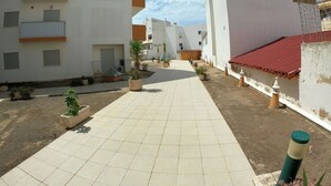 A courtyard with tiled flooring, potted plants, and white buildings with balconies. - Algarve, T2 apartment w/balcony, Armação de Pera (Armação de Pêra)