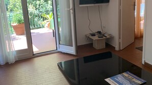 Una habitación con puerta de vidrio corredera que da a un balcón, un televisor de pantalla plana en la pared y una mesa con una revista.