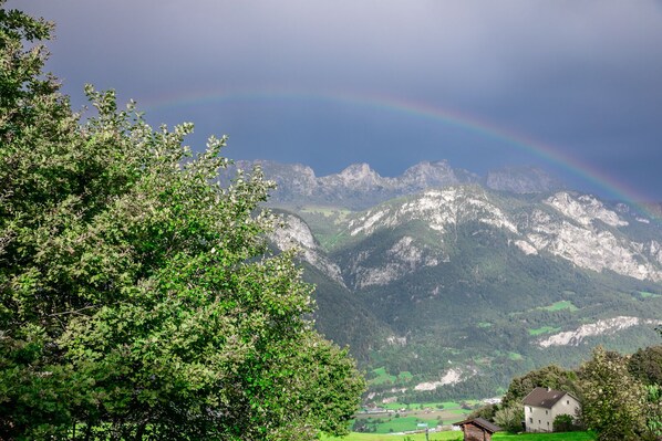 A mountain landscape with a rainbow, a tree, and a house.
