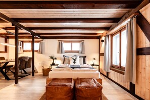 A cozy bedroom with a wooden ceiling, a large bed with pillows, a chair, and a table with a lamp.