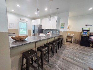 A modern kitchen with a granite countertop, stainless steel appliances, and a bar area with stools.