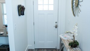 Un couloir avec une porte blanche, un banc en bois orné d’un vase de fleurs et un élément décoratif fixé au mur.