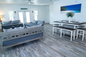 A room with a bed, a dining table set for four, and a view of the ocean through a window. - Coastal Elegance Villa & Pool Sleeps 18 (Panama City Beach)