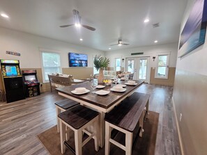 A dining area with a long table set for four, a ceiling fan, and a mounted television.