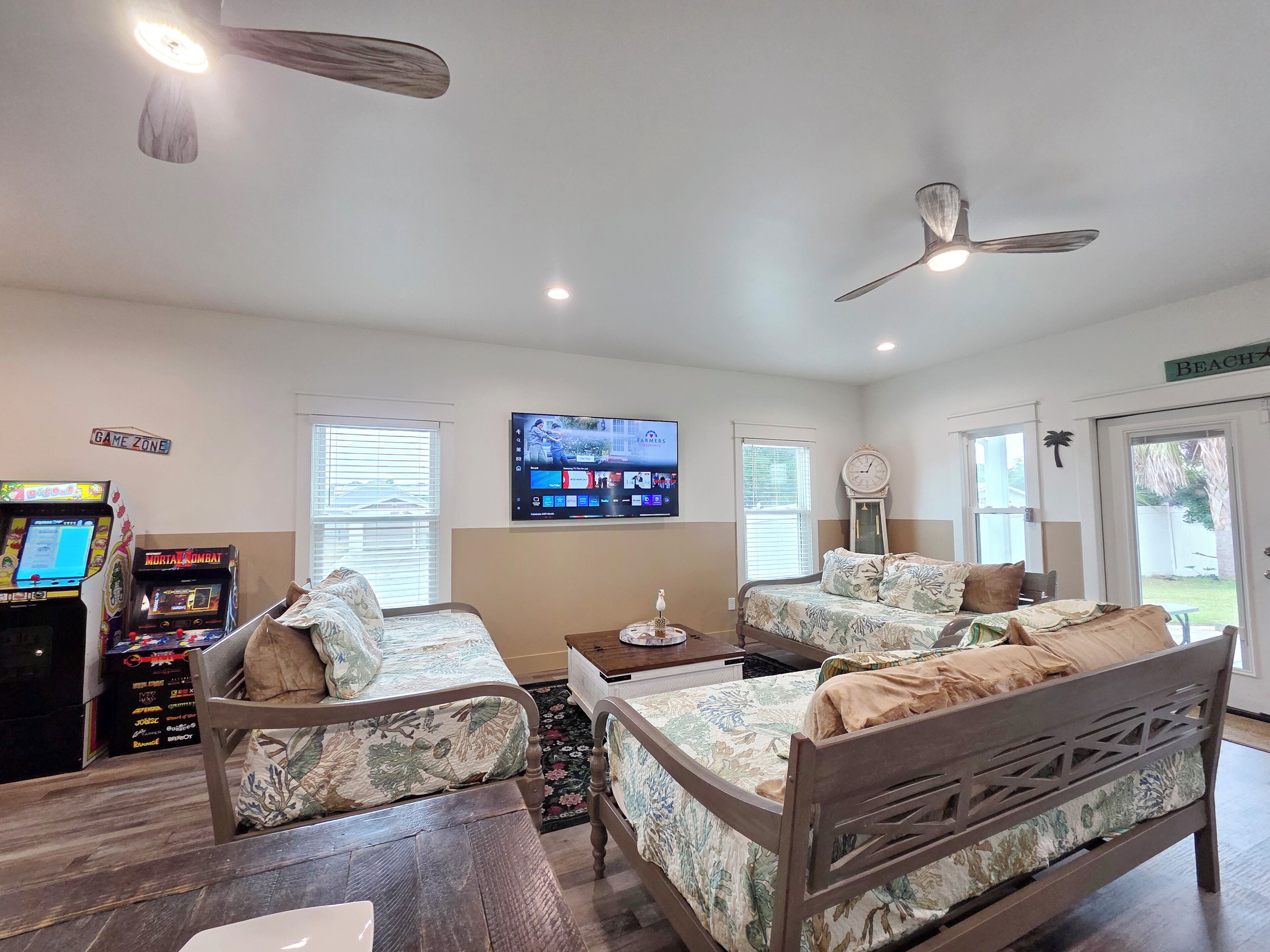 A room with two beds, a television, ceiling fans, and arcade games.