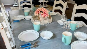 A dining area with a table set for four, surrounded by white chairs, a chandelier, and a ceiling fan.