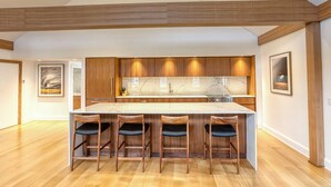 A modern kitchen with a central island, wooden bar stools, and a high ceiling with exposed beams. - The Penthouse, Downtown Lenox by Evergreen Home (Lenox)