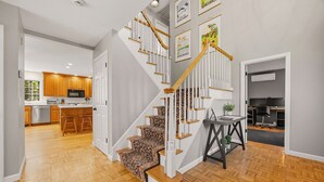 A modern interior with a wooden staircase, a kitchen with wooden cabinets, and a dining area with a bar. - Berkshires Colonial on 2 Acres by Evergreen Home (Pittsfield)