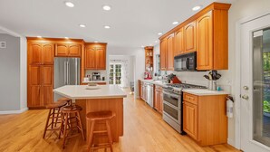 A modern kitchen with wooden cabinets, stainless steel appliances, and a central island with bar stools. - Berkshires Colonial on 2 Acres by Evergreen Home (Pittsfield)