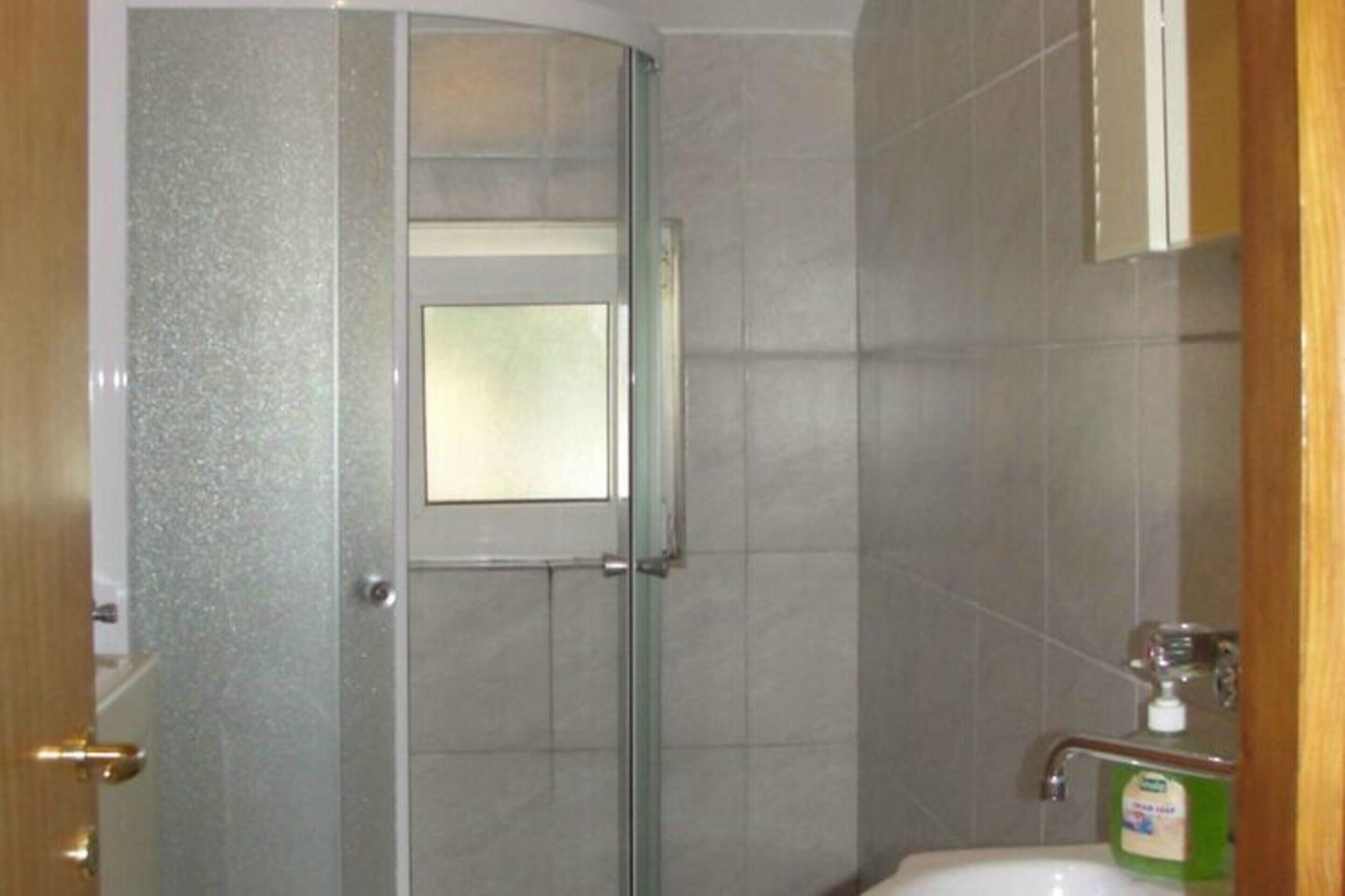 Une salle de bain avec une porte de douche en verre, un lavabo avec un distributeur de savon et un miroir au-dessus du lavabo.