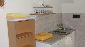 A compact kitchen with a sink, a stove, and a countertop. There are shelves above the sink holding dishes and glasses. - Apartments Pinija - Standard Two Bedroom Apartment With Balcony - (Supetar)