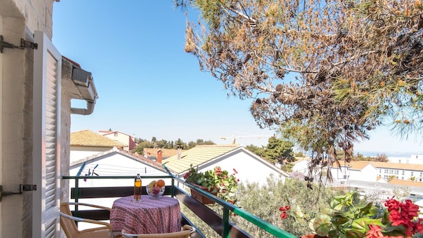 A balcony with wicker chairs, a table with a patterned tablecloth, and potted plants. - Apartments Pinija - Standard Two Bedroom Apartment With Balcony - (Supetar)