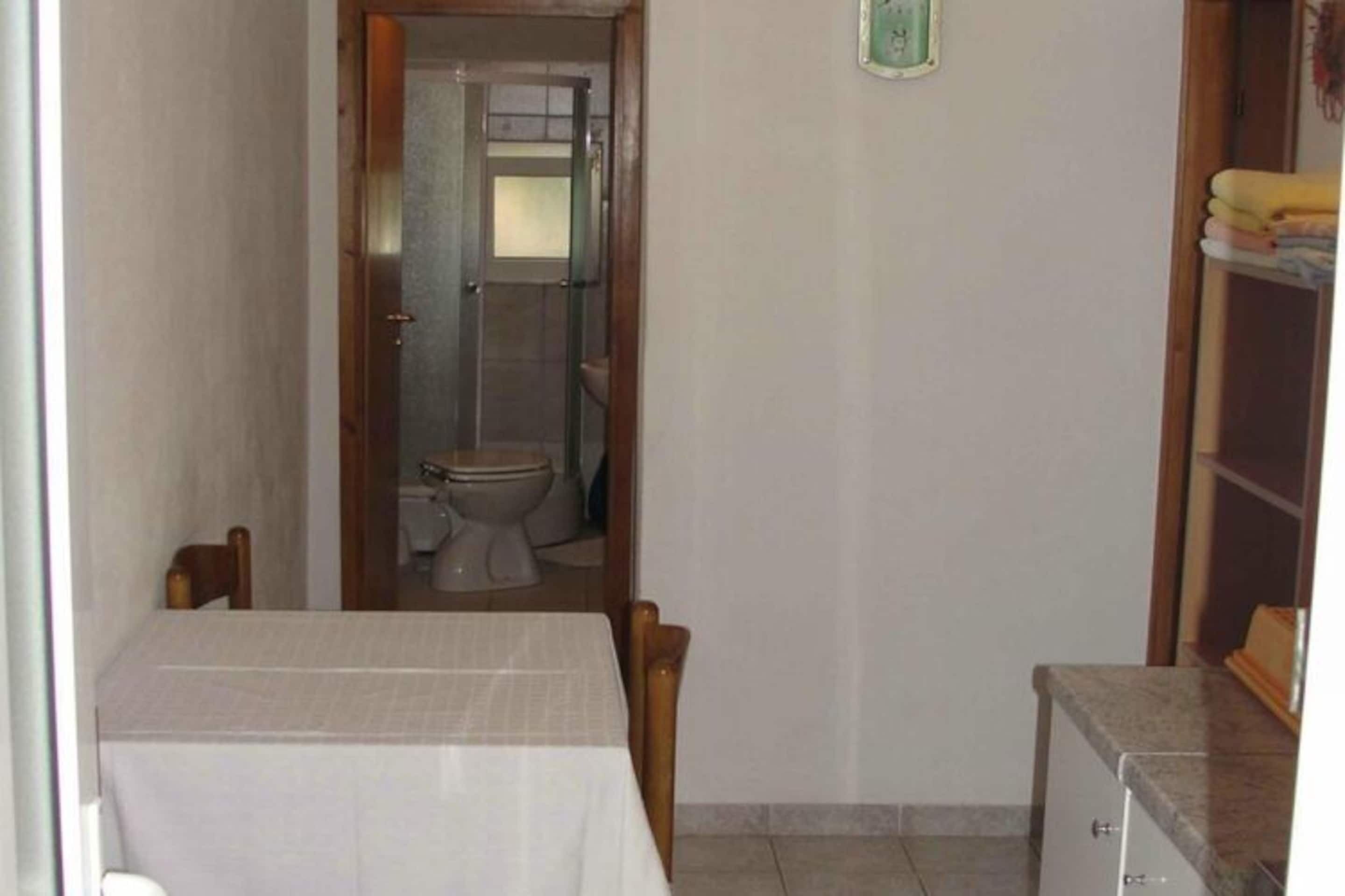 Ein kleines, schlichtes Zimmer mit einem Einzelbett, einem Nachttisch und einem Fenster.
