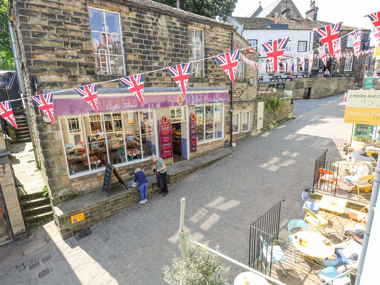 A stone building with a coffee shop and bakery on the ground floor, featuring outdoor seating and British flags.