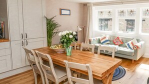 A dining area with a wooden table and chairs, a vase with flowers, a sofa with cushions, and a window with stained glass. - Piccadilly View (Keighley)