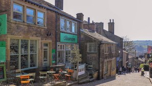 A cobblestone street with a brick building labeled "The Classroom" featuring outdoor seating and a signboard. - Piccadilly View (Keighley)