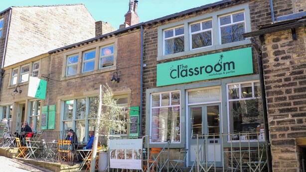 A row of buildings with a green sign for 'The Classroom' indicating workshops and parties. - Piccadilly View (Keighley)