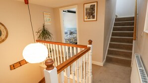 A staircase with a wooden handrail and white balusters, leading to a bedroom with a bed and a wall-mounted clock. - Piccadilly View (Keighley)