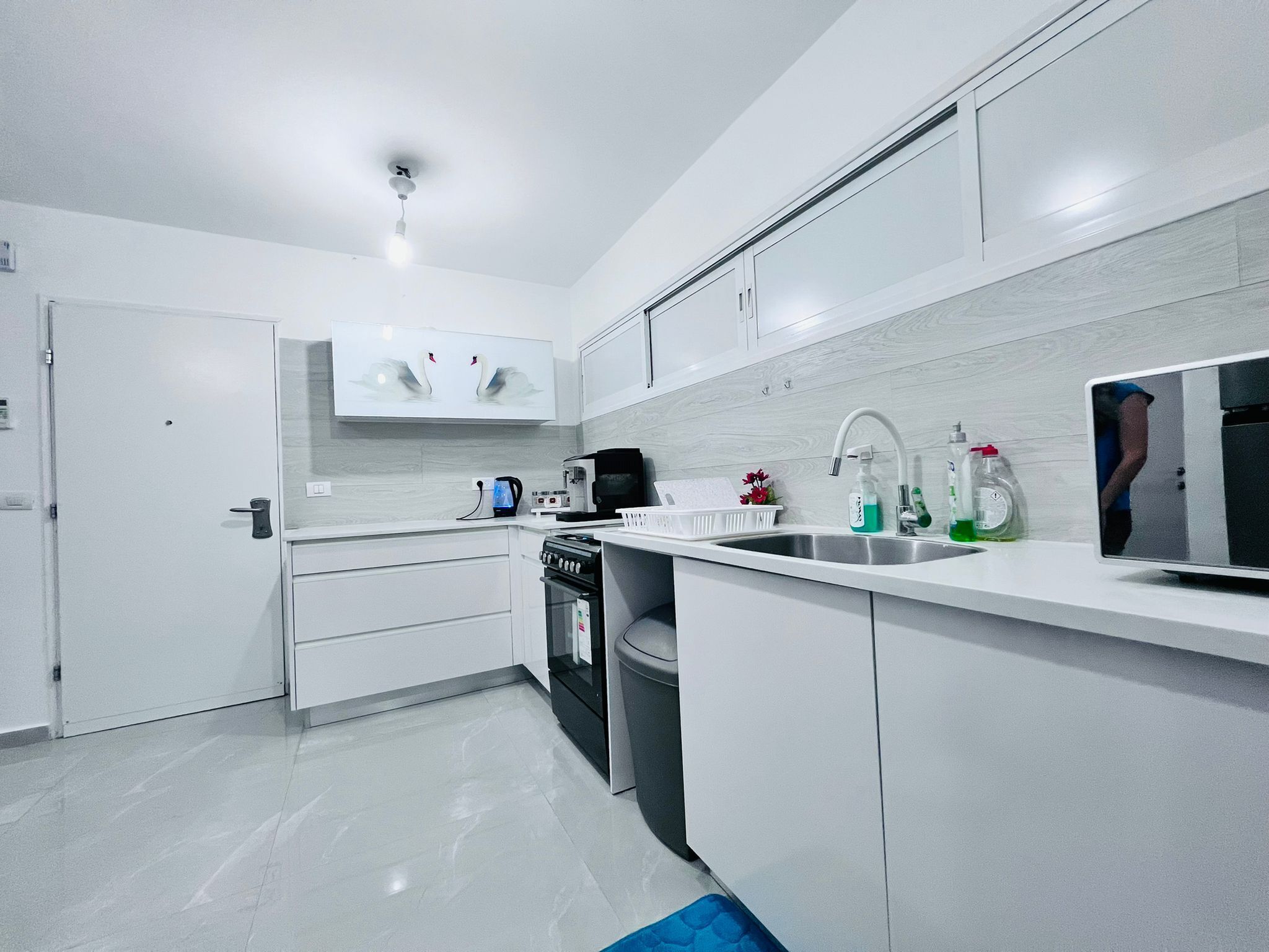 A modern kitchen with white cabinetry, a built-in oven, a coffee maker, and a sink with soap dispensers.