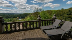A wooden deck with a stone balustrade overlooking a scenic landscape with trees and a lake. - Castle in Spa With Lake View & Heated Pool (Jalhay)