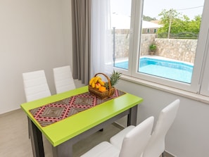 A dining area with a table set for four, a pool view, and a stone wall. - Villa Kabalero - Four-bedroom Villa With Private Pool (Konavle)