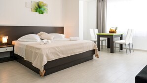 Ein modernes Hotelzimmer mit einem großen Bett, einem Esstisch mit Stühlen und einem Fenster mit Vorhängen.