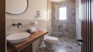 Ein Badezimmer mit einem Holzkosmetikschrank, einem weißen Waschbecken, einer Toilette und einem Duschbereich mit gemusterten Fliesen.