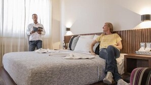 Ein Hotelzimmer mit einem großen Bett, zwei Nachttischlampen, einem Holz-Kopfteil und einem Fenster mit durchsichtigen Vorhängen.