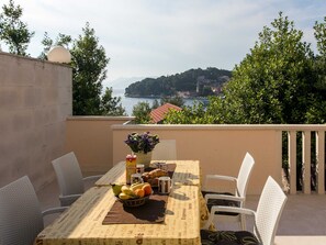 A table set with fruits, pastries, and coffee cups, overlooking a coastal town and sea.