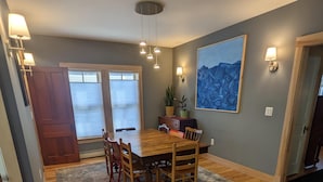 Un comedor con una mesa y sillas de madera, un tapete estampado y un ventanal con persianas.