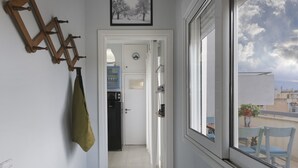 Un pasillo estrecho con un perchero de madera, una puerta que da a una habitación con ventana, y vistas de edificios al exterior.