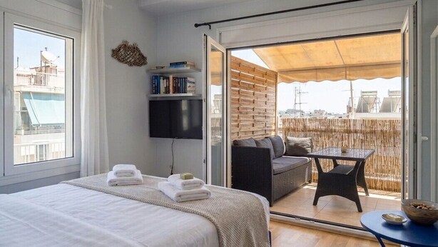 Un dormitorio con cama, televisor, estantería y balcón con mesa y sillas.
