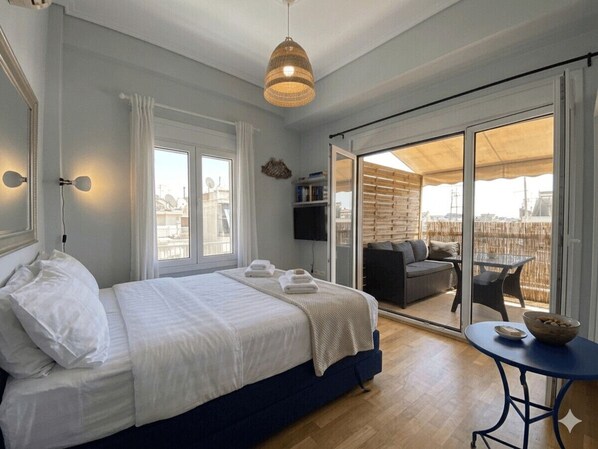 A bedroom with a bed, a TV, a balcony with seating, and a view of the city.