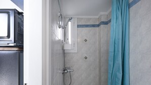 Un espacio de ducha pequeño y cerrado, con cabezal de ducha y un rociador de mano, además de un inodoro.
