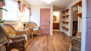 A cozy room with wicker furniture, a pink door, and wooden shelves. - Quaint 3-bedroom cottage in Nashville, shopping, and dining! Pet-friendly! (Nashville)