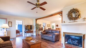 A living room with a fireplace, leather sofa, wooden coffee table, and a ceiling fan. - Quaint 3-bedroom cottage in Nashville, shopping, and dining! Pet-friendly! (Nashville)