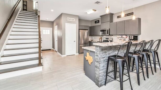A modern kitchen with a central island, bar stools, and a staircase leading to another level.