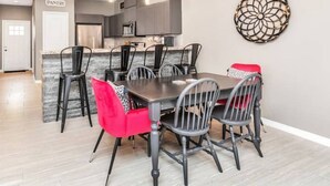A modern kitchen with grey cabinets, a central island, and a dining area with black chairs and a red chair.