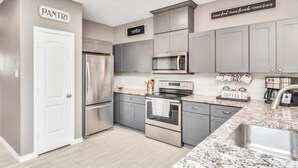 A modern kitchen with grey cabinets, stainless steel appliances, and a granite countertop.
