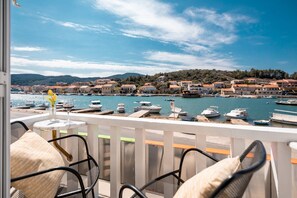 Ein Balkon mit Korbstühlen und einem Tisch, mit Blick auf einen Hafen voller Boote und eine Küstenstadt.