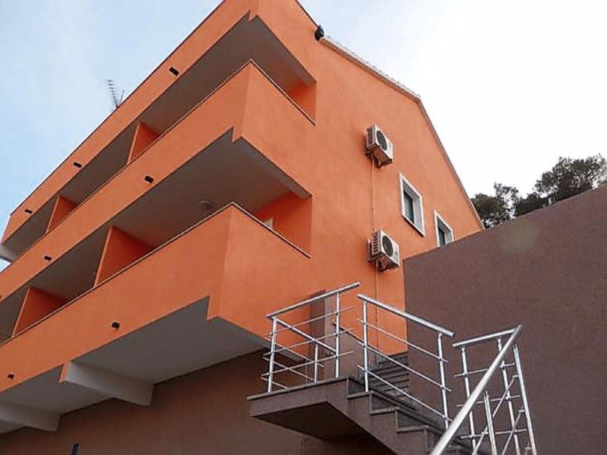 A multi-story building with a distinctive orange facade, external staircases, and air conditioning units.