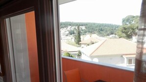 A balcony with a table and chair, a view of houses and trees, and a window with a curtain. - Apartments St Rialto - Comfort One-Bedroom Apartment with Balcony and Sea View (Jelsa)