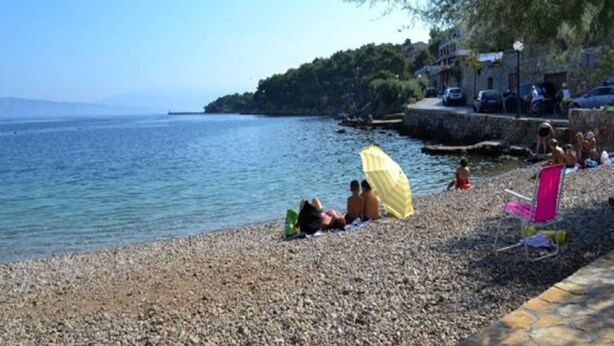 A pebbled beach with people relaxing under umbrellas, a clear sky, and a distant view of a coastline with buildings. - Apartments St Rialto - Comfort One-Bedroom Apartment with Balcony and Sea View (Jelsa)