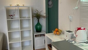 A modern kitchen with white cabinets, a green accent wall, a small side table with a vase, and a countertop with a kettle and toaster. - Apartment Fresh Start- One Bedroom Apartment (Zadar)