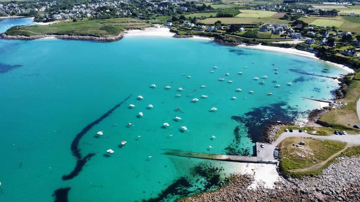 Luchtbeeld van een kustgebied met bootjes in turquoise water, een zandstrand en een klein pier.