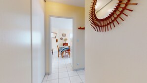 A hallway leading to a dining area with a white tiled floor, a wooden dining table with chairs, and a wall-mounted wooden spiral decoration.
